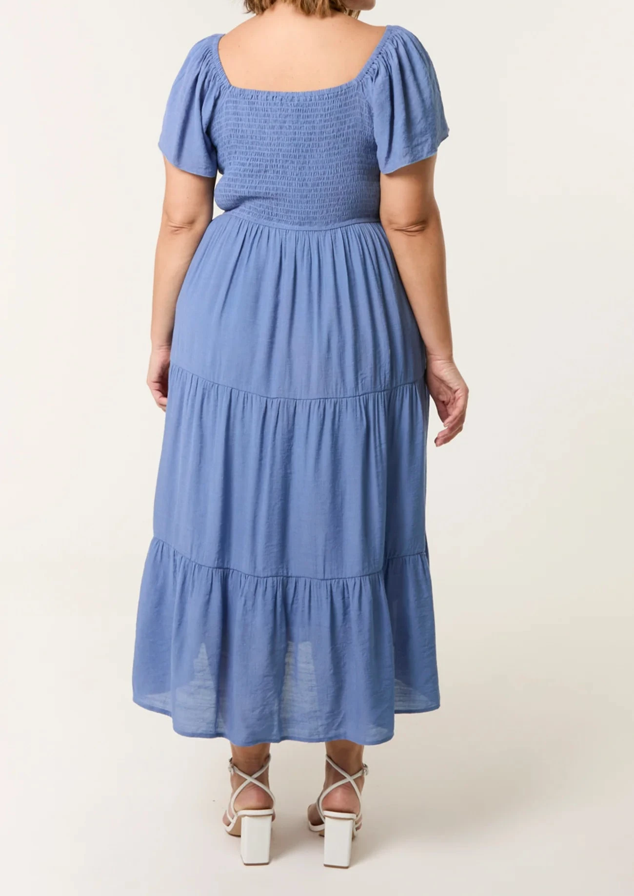 Woman wearing a blue dress with ruffled sleeves and bottom hem on a white background