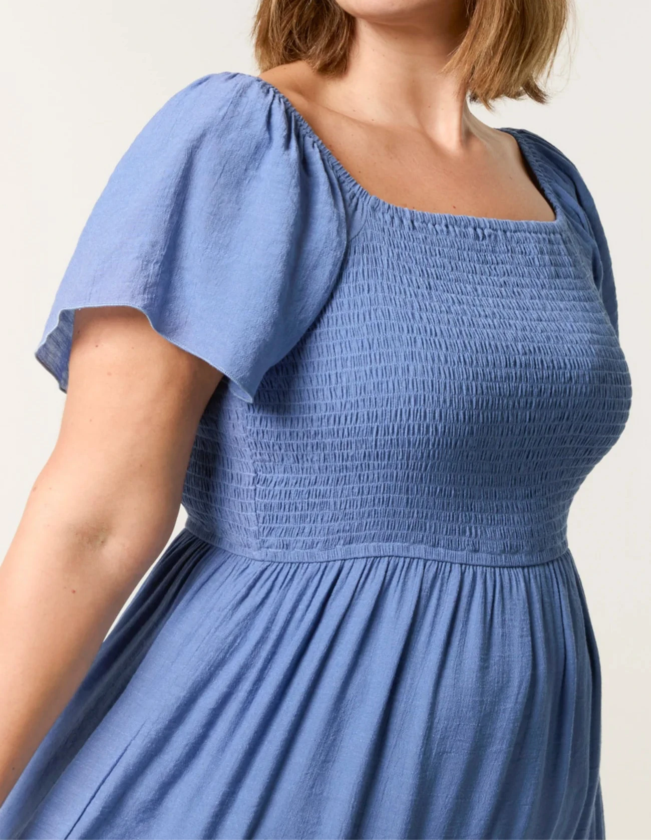 Woman wearing a blue smocked dress against a plain background